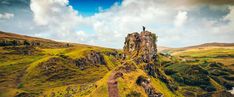 a man standing on top of a tall rock in the middle of a lush green field