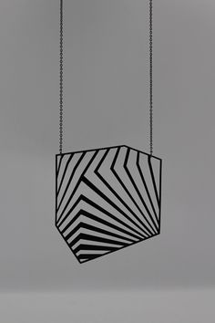 a black and white geometric object hanging from a chain on a gray background with room for text