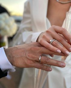 the bride and groom are holding their wedding rings on their fingers as they hold each other's hands