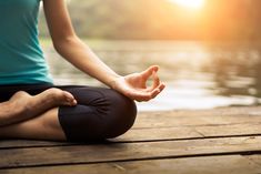 a woman is sitting in the lotus position with her hands open and looking at the water