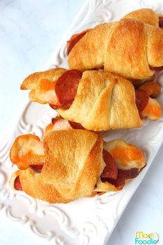 two hot dogs wrapped in croissants are on a white plate next to another sandwich