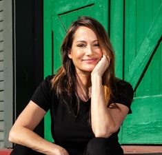 a woman sitting in front of a green door with her hand on her chin and looking at the camera