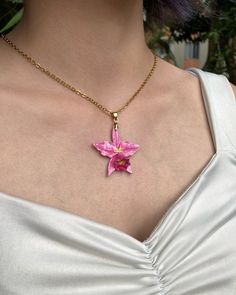 a woman wearing a necklace with a pink flower on it's back and gold chain