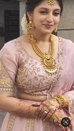 a woman in a pink lehenga with gold jewelry on her neck and hands