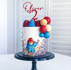 a birthday cake is decorated with balloons and a teddy bear on the top, which reads silver 2