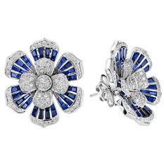 Shine bright with these stunning diamond and sapphire earrings. The earrings features 146 round cut diamonds and 96 French cut blue sapphires. These magnificent and timeless earrings would add a touch of grace and elegance to any occasion! Earrings Information Style: Art Deco Metal: 18K White Gold Width: 23 mm. Length: 26 mm. Weight: 17.70 g. (approx. in total) Backing: Push Back Gemstones I Type: Diamond Shape: Round Average Color: H Average Clarity: SI Size: 1 - 1.3 mm. Number: 146 Weight: 1.0 Branded Earrings, Sapphire Diamond Earrings, Diamond Tops, Blue Sapphire Jewelry, Timeless Earrings, Art Deco Metal, Sapphire And Diamond Earrings, Floral Studs, Earring Box