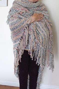 a woman standing in front of a white wall wearing a multicolored shawl