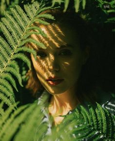 a woman standing in front of green leaves with the sun shining on her face and shoulders