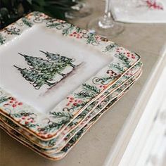 a stack of christmas themed plates sitting on top of a counter next to wine glasses