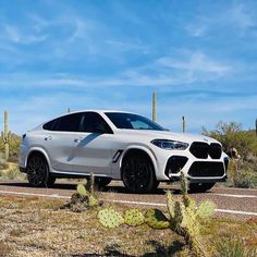 a white bmw suv parked on the side of a road in front of cacti