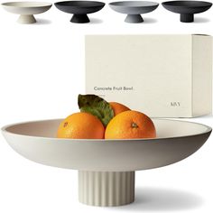 four oranges sitting in a bowl on top of a white plate with black handles