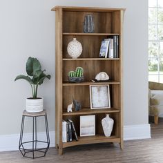 a wooden bookcase with books and pictures on it next to a potted plant