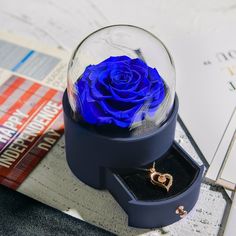 a blue rose in a glass dome on top of a table next to a book