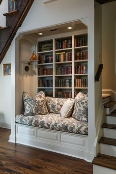 a couch sitting under a stair case next to a book shelf with books on it