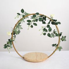 a wooden circle with white roses and greenery on it, sitting on a table