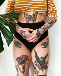 a woman with tattoos on her body standing next to a plant