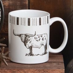 a white coffee mug with an image of a cow on it next to a clock