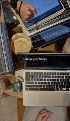 two laptops sitting on top of a wooden table next to coffee cups and mugs