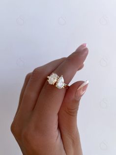 a woman's hand holding a ring with two diamonds on it and the middle finger