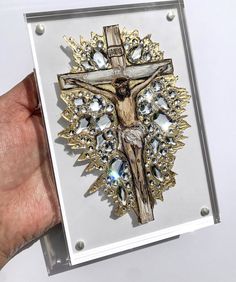 a hand holding up a glass box with a cross on it and some jewels around the edges