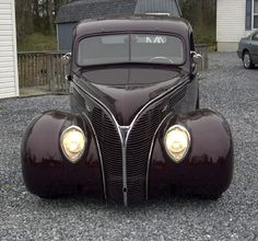 an antique car parked on gravel in front of a house