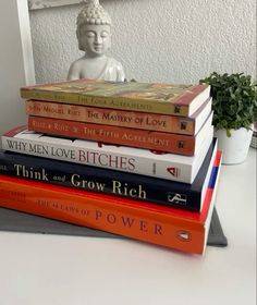 a stack of books sitting on top of a white table next to a buddha statue