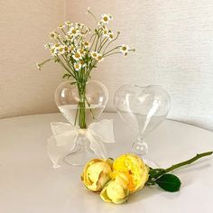 two clear vases with flowers in them on a white tableclothed surface next to each other