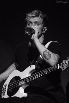 a man holding a beer in his mouth while sitting on a chair with a guitar