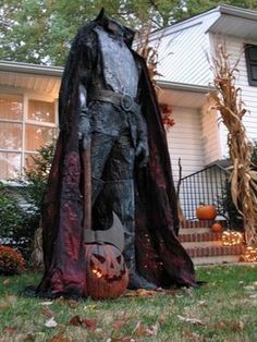 a scarecrow statue in front of a house with pumpkins on the lawn and trees