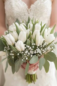 a bride holding a bouquet of white tulips and baby's breath