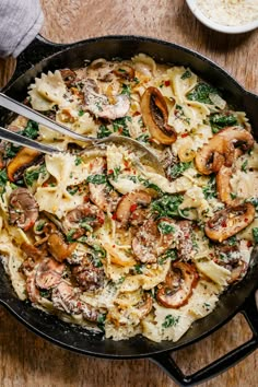 a skillet filled with pasta, mushrooms and spinach on top of a wooden table