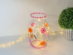 a glass vase with flowers on it next to a potted plant and string lights