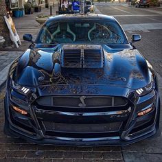 the front end of a black sports car parked on a city street with graffiti all over it