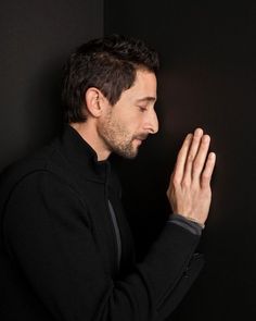 a man standing in front of a black wall holding his hands together and looking at something