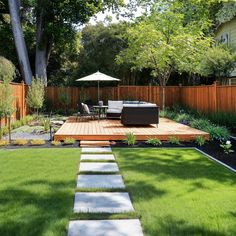 a wooden deck in the middle of a yard next to a lawn with chairs and an umbrella