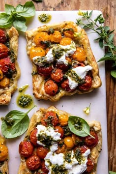 four small pizzas with tomatoes, cheese and basil on them sitting on a tray