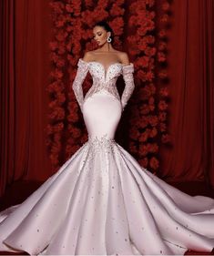 a woman standing in front of red roses wearing a white gown with long sleeves and beading