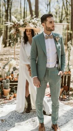 a man in a green suit and bow tie standing next to a woman wearing a white dress