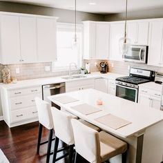 a kitchen with white cabinets and an island in the middle, surrounded by bar stools