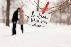 a couple standing in the snow next to a tree with a sign hanging from it