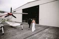 a bride and groom walking towards an airplane in front of a hangar at their wedding