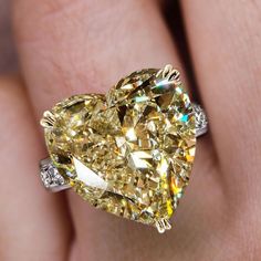 a fancy yellow diamond ring on someone's finger with the center stone in the shape of a heart