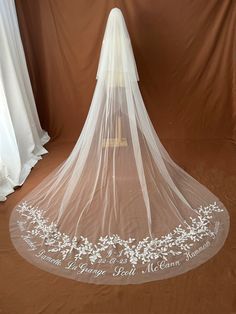 a wedding veil with white flowers and leaves on the bottom is shown in front of a brown backdrop