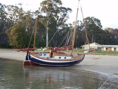 a small sailboat sitting on top of a beach next to the ocean with trees in the background