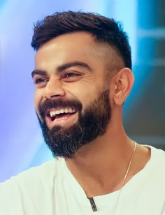 a man with a beard smiling and wearing a necklace