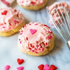 some cookies with pink frosting and sprinkles on a table next to a whisk