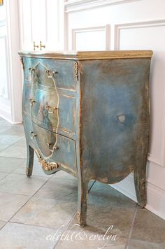 an old blue dresser is sitting on the floor in front of a white wall and tile floor