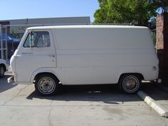 an old white delivery truck parked in a parking lot next to a fence and building