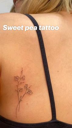 the back of a woman's shoulder with a small flower tattoo on her left side