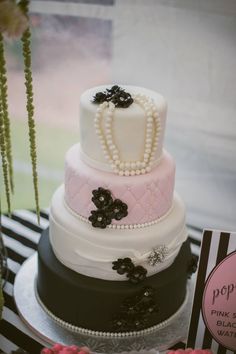 a three tiered cake is decorated with pearls and black flowers on a table in front of a window